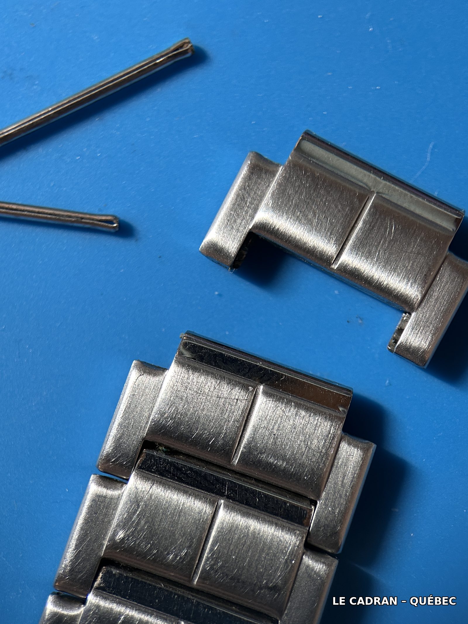 Maillon retiré du bracelet, avec la goupille et le ressort visibles à côté